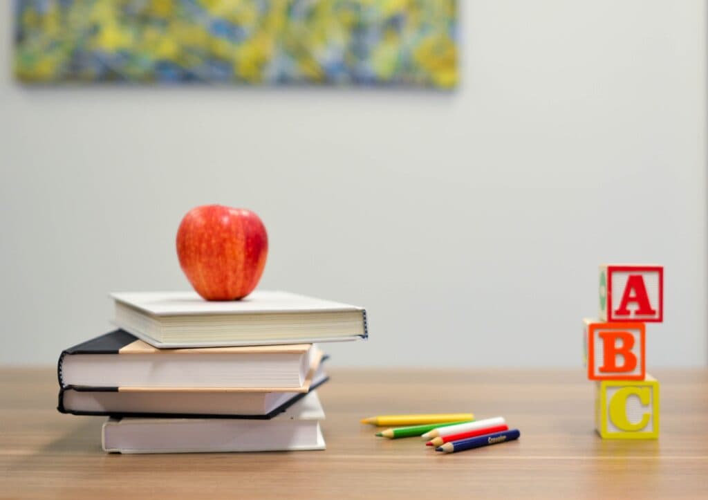 stack of books with an apple on top, colored pencils, and ABC blocks on a table.