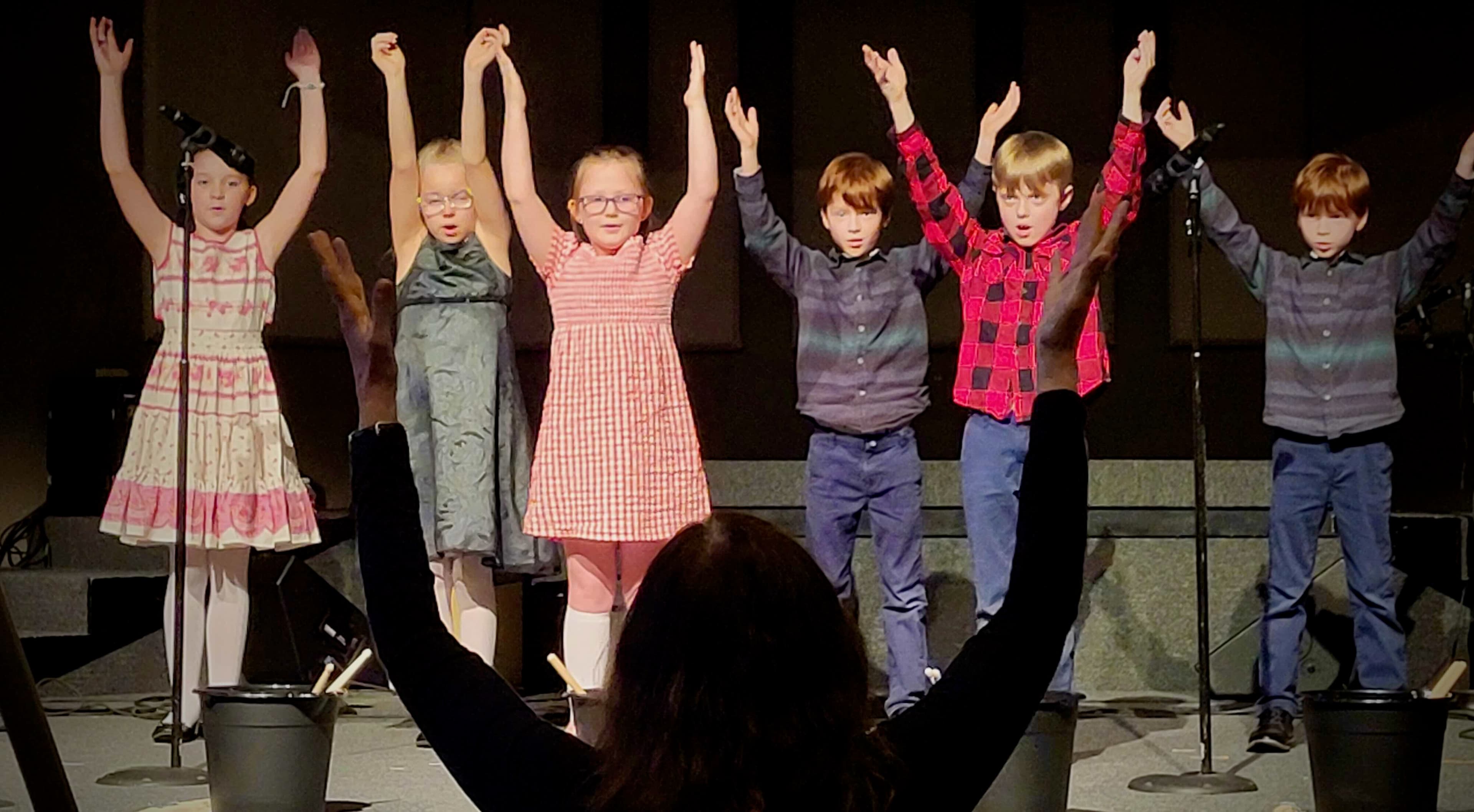 Kardia students on stage raising hands during performance.