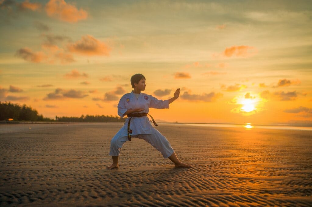Child in martial arts pose on beach with sunset