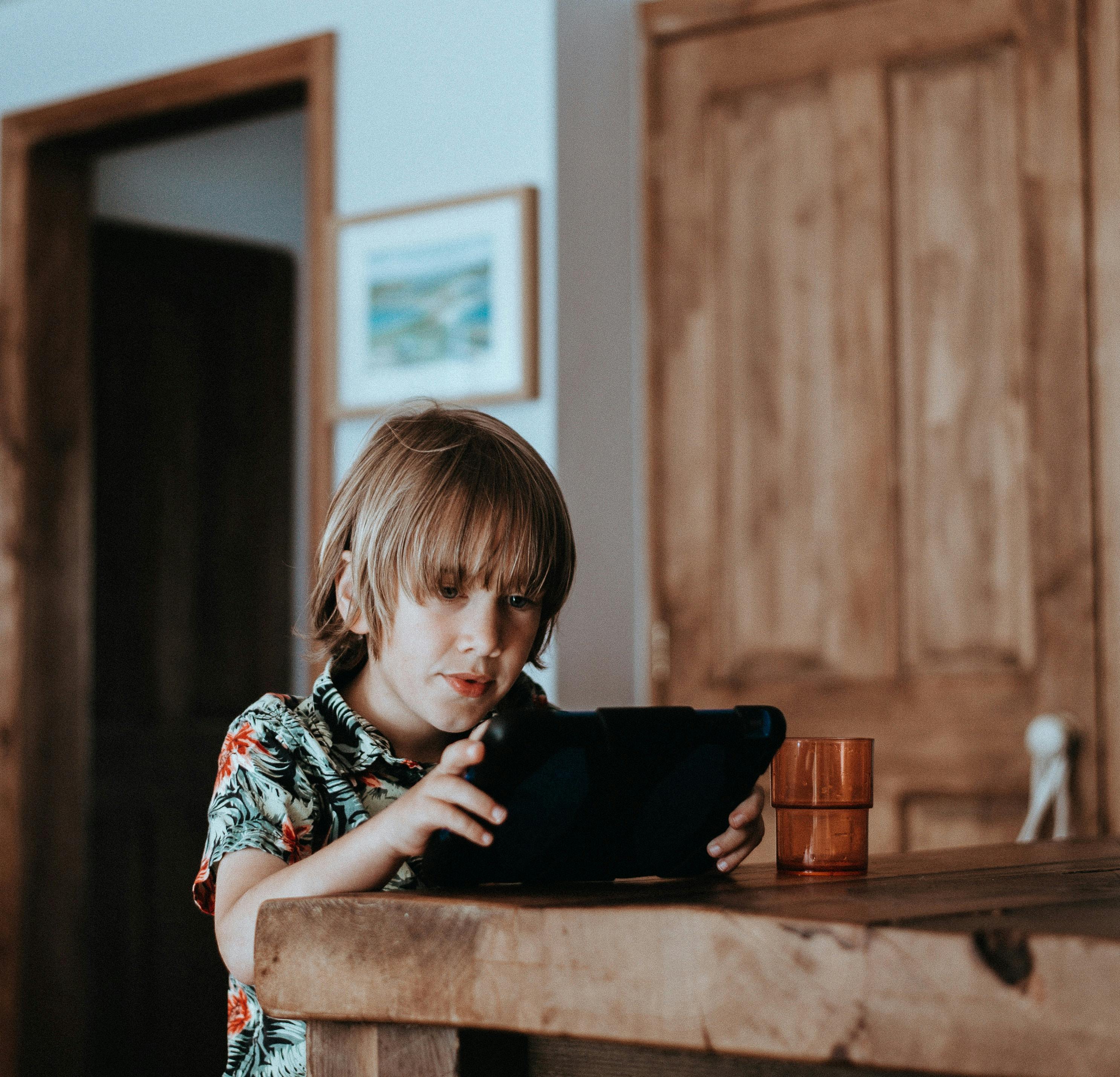 Child sitting at counter looking at a tablet with a beverage sitting next to him.