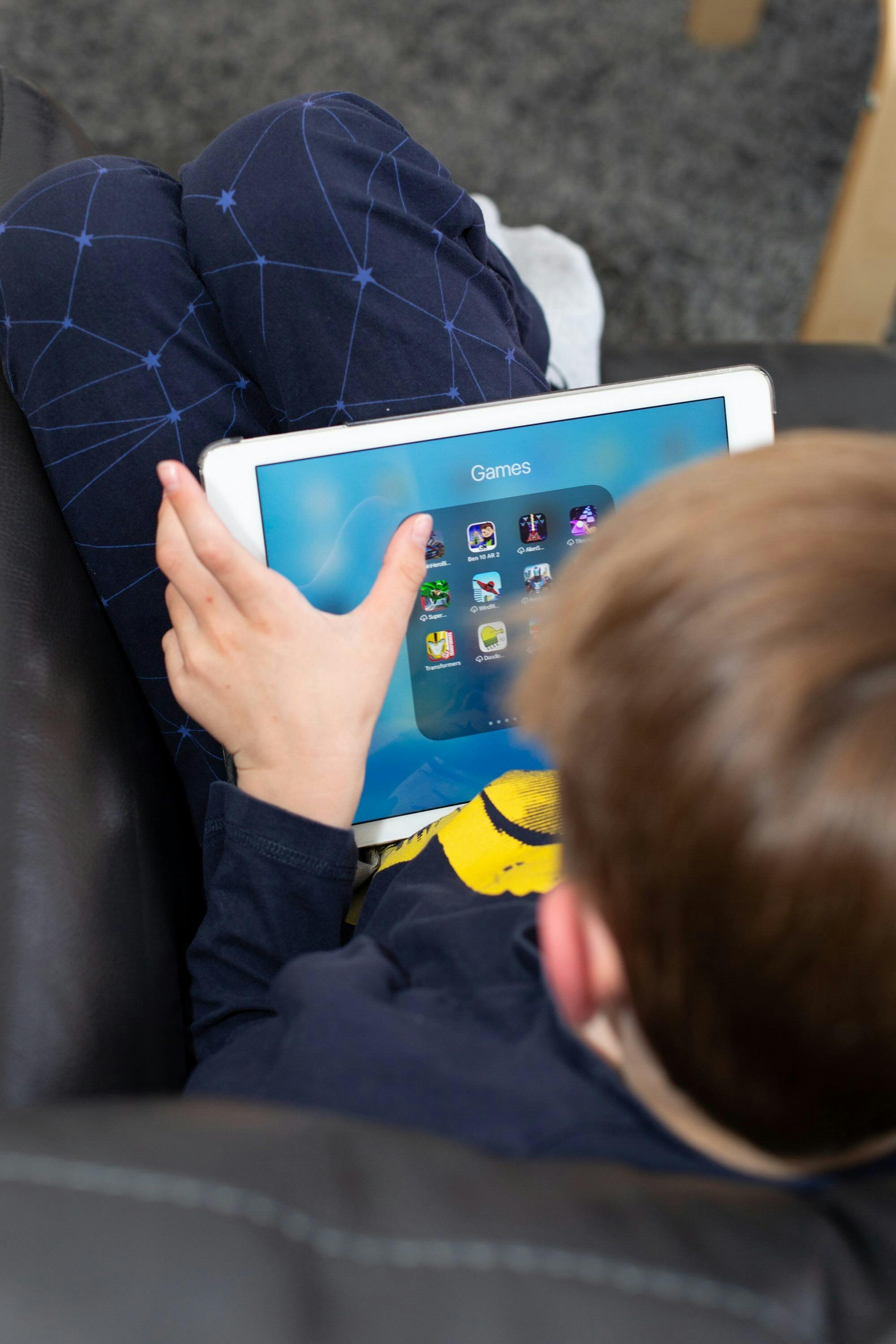 Young child sitting with tablet. He is looking at a menu of games to play.