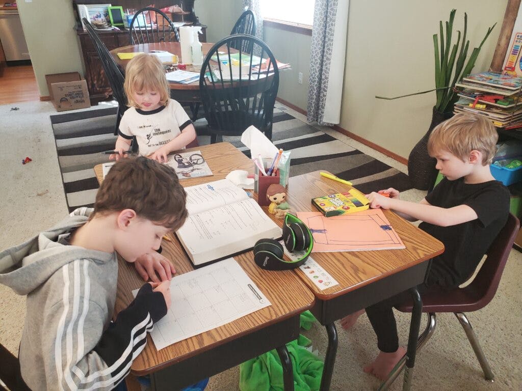 Three students of various ages working on school work at kitchen table.